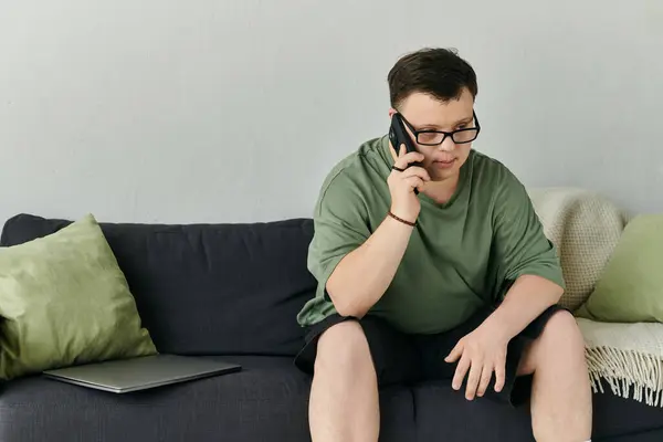 A thoughtful young man with Down syndrome speaks on the phone while sitting comfortably at home. — Stock Photo
