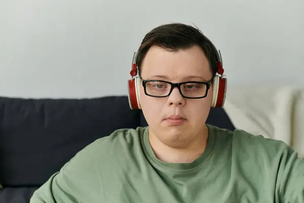 A young man with Down syndrome relaxes at home, listening to music through headphones. — Stock Photo