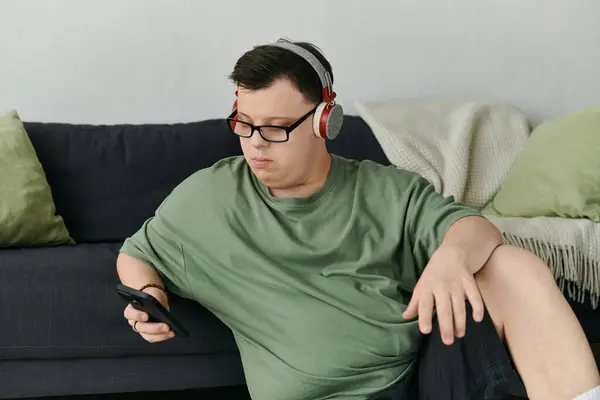 A young man with Down syndrome listens to music while sitting comfortably on a couch. — Stock Photo