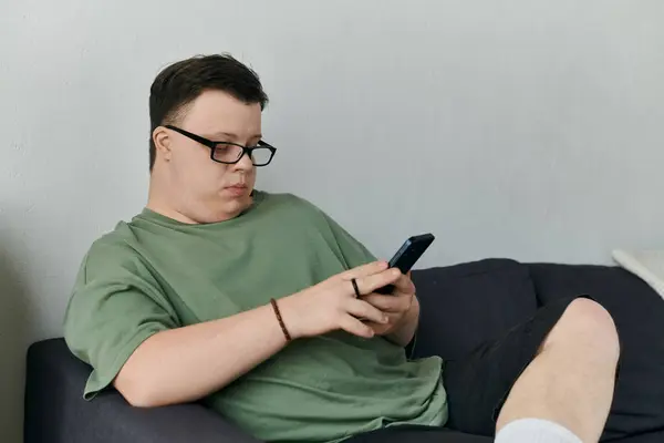 A young man with Down syndrome engages with his smartphone comfortably on a couch. — Stock Photo