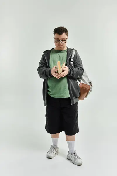 A young man with Down syndrome reads a book while standing comfortably at home. — Stock Photo