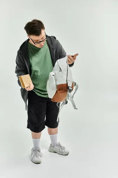A young man with Down syndrome explores his backpack and holds a book at home. — Stock Photo
