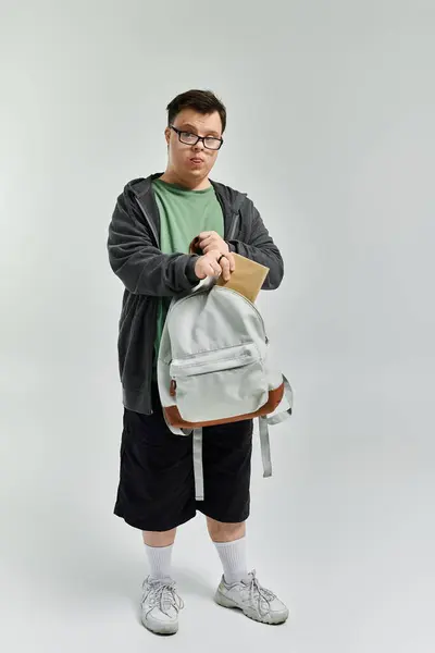 A young man with Down syndrome prepares to head out, holding his backpack with a determined look. — Stock Photo