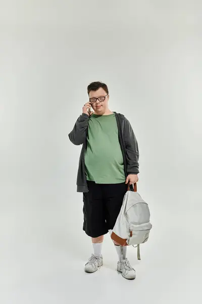 A young man with Down syndrome at home speaks on the phone with a backpack in hand. — Stock Photo
