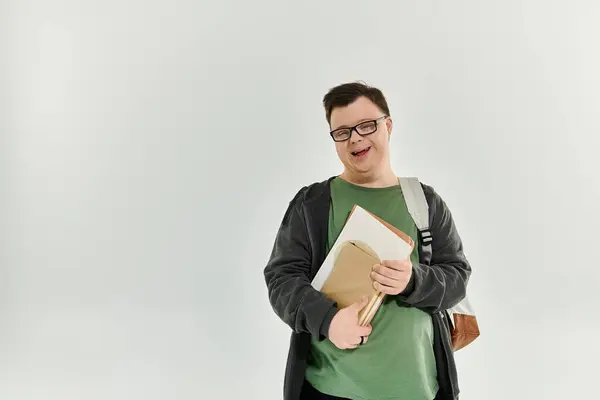 A cheerful man with Down syndrome stands at home, holding books and smiling warmly. — Stock Photo
