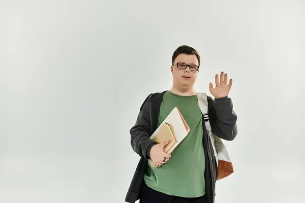 A young man with Down syndrome greets warmly while holding books at home. — Stock Photo