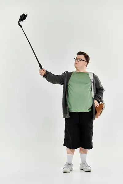 A young man with Down syndrome stands confidently taking a selfie with a stick. — Stock Photo