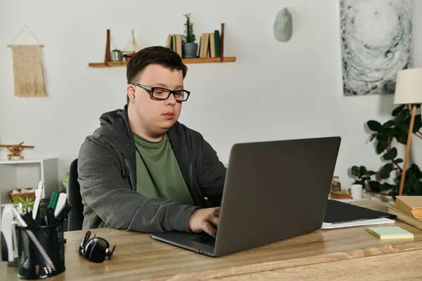 Engagierter junger Mann mit Down-Syndrom arbeitet intensiv am heimischen Schreibtisch am Laptop. — Stockfoto