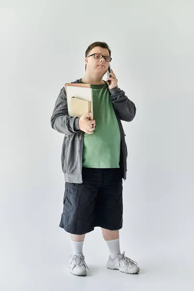 A young man with Down syndrome chats on the phone while holding a folder at home. — Stock Photo