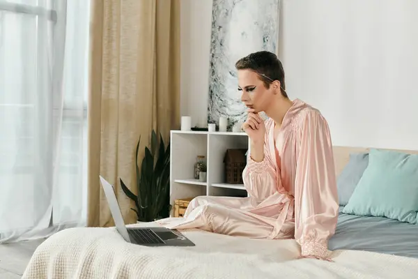 An attractive drag queen intently studies a laptop while seated on a cozy bed. — Stock Photo