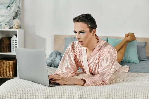 A vibrant drag queen is focused on their laptop while lounging on a bed. — Stock Photo