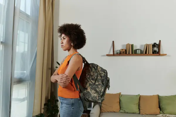 Una joven vestida casualmente con un suéter vibrante mira pensativamente desde la ventana de una sala de estar. — Stock Photo