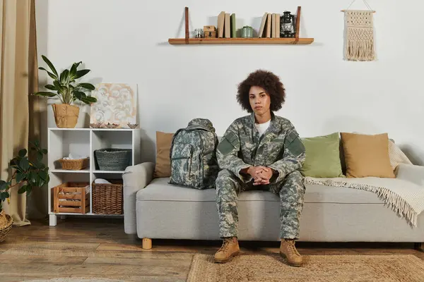 Una joven afroamericana en equipo militar se sienta pensativamente en su sala de estar, lista para ser desplegada. — Stock Photo