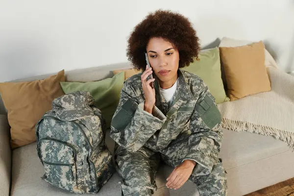 Una joven en uniforme militar se sienta pensativamente en un sofá, preparándose para su servicio. - foto de stock