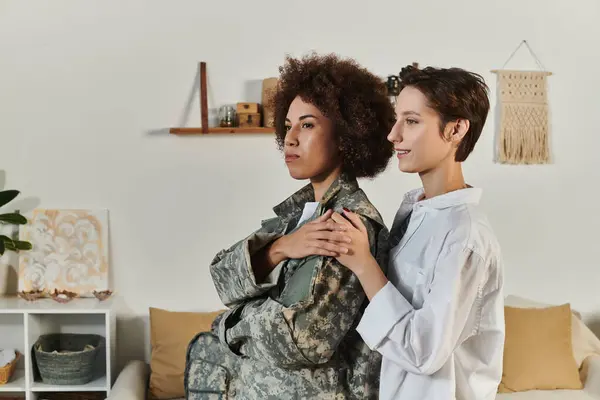 A soldier in camouflage bids farewell to her wife in a heartfelt moment at home. — Stock Photo
