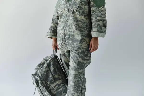 Um jovem soldado dedicado está confiante em equipamento de camuflagem, pronto para o serviço com uma mochila na mão. — Fotografia de Stock