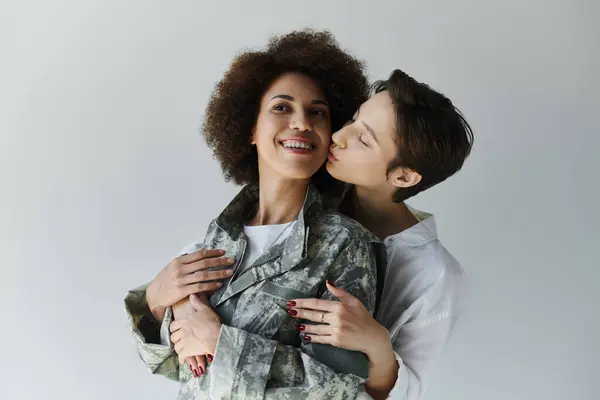 Un soldado en uniforme de camuflaje comparte un momento amoroso con su esposa en un cálido ambiente de estudio. - foto de stock