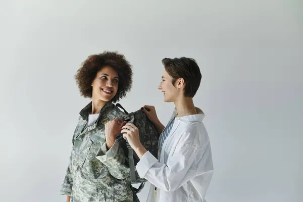 Un soldado en camuflaje se prepara para el despliegue mientras su esposa ofrece apoyo y amor. — Stock Photo