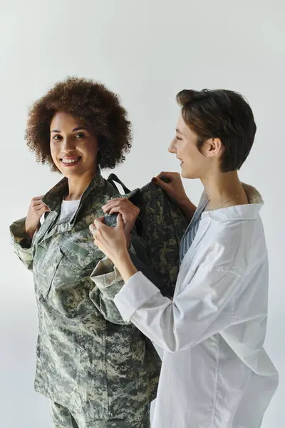 Un soldado militar camuflado recibe una cariñosa despedida de su esposa en un contexto gris. — Stock Photo