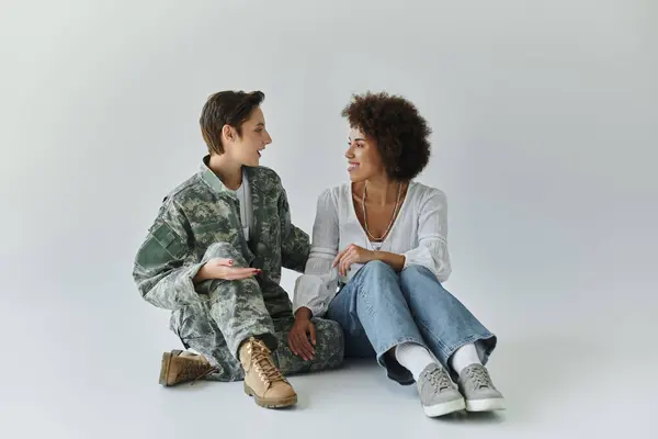 Un soldado en uniforme de camuflaje comparte un momento amoroso con su esposa en un acogedor estudio. — Stock Photo