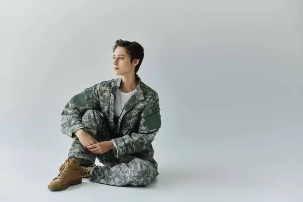 Mulher se prepara para o serviço militar em um estúdio com um pano de fundo cinza. — Fotografia de Stock