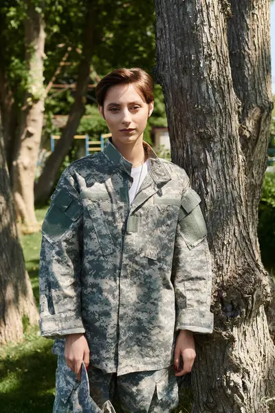 Un joven soldado en camuflaje se levanta orgullosamente al aire libre, abrazando el calor del hogar después del servicio. - foto de stock