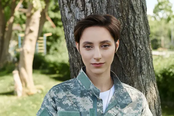 Una joven con un uniforme de camuflaje se para al aire libre, sonriendo cuando regresa a casa del servicio militar. — Stock Photo
