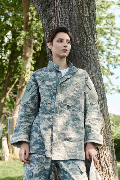A young woman in a camouflage uniform stands outdoors, reflecting on her return home from military service. — Stock Photo