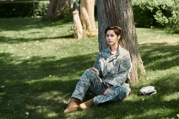 A young soldier in camouflage rests against a tree, reflecting on home after returning from service. — Stock Photo