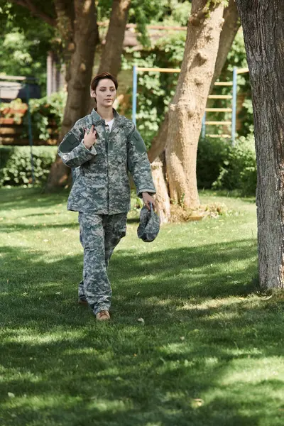 Un joven soldado en uniforme de camuflaje camina con confianza a través de un espacio verde al aire libre, abrazando el regreso a casa. — Stock Photo