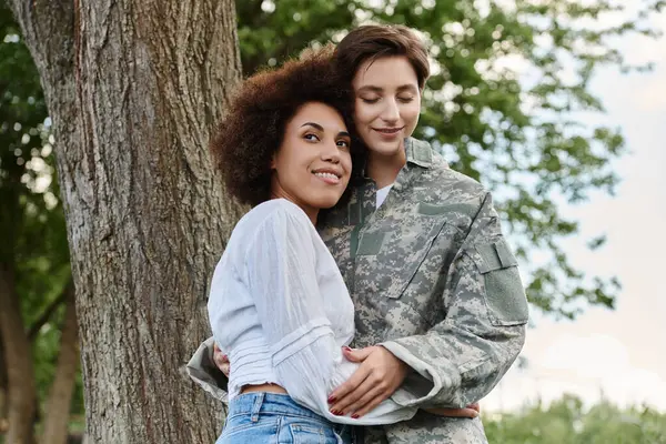 Una giovane soldato in camuffamento è gioiosamente accolta a casa da sua moglie, che celebra il loro amore all'aperto.. — Foto stock