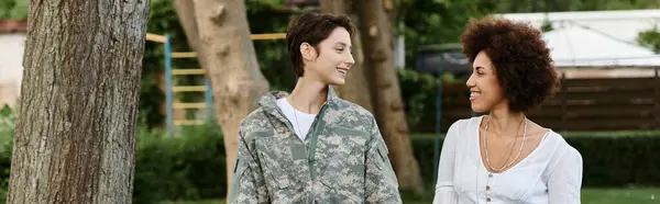 Una joven soldado camuflada se reúne alegremente con su esposa en un cálido y acogedor abrazo. - foto de stock