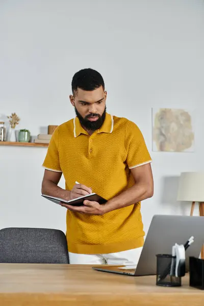 A man with a focused expression writes notes while standing at his desk. — Stock Photo