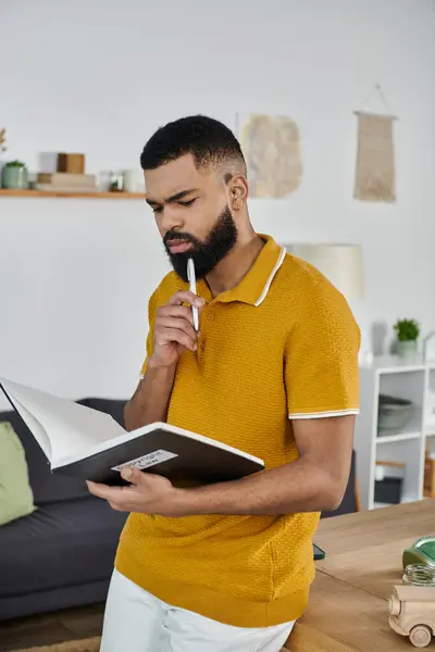 A man in a mustard shirt contemplates while reading a notebook at home. — Stock Photo