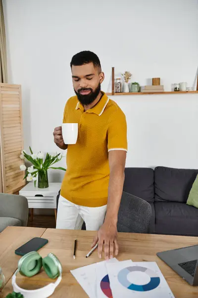 Un uomo elegante sorseggia caffè ed esamina i documenti in un home office ben decorato. — Foto stock