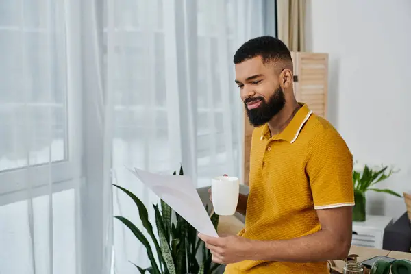 Man relaxes indoors, sipping coffee while reading quietly by the window. — Stock Photo