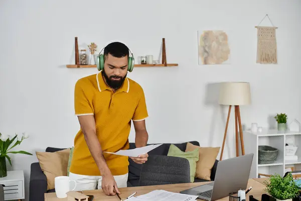 A man reviews papers while wearing headphones, focused on his tasks at home. — Stock Photo