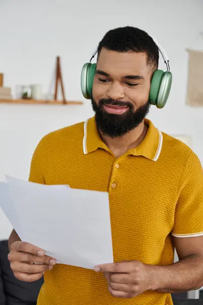 Entspannter Mann mit Kopfhörer lächelt, während er zu Hause Papiere studiert. — Stockfoto