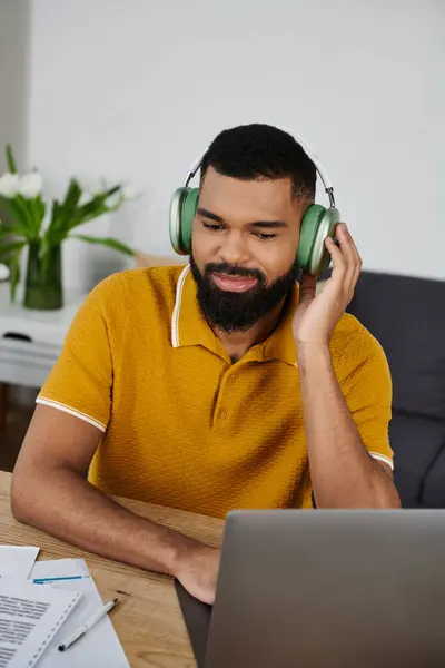 A handsome man wearing headphones enjoys music at home while focused on his task. — Stock Photo