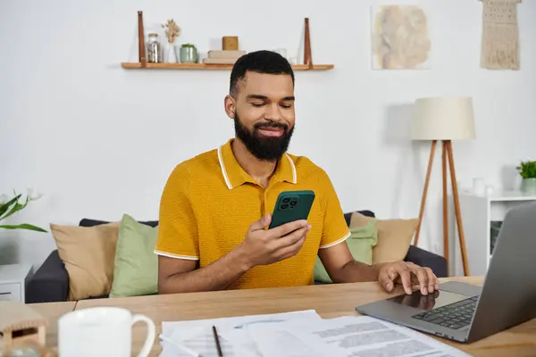 Smiling man relaxes at home while using his phone and working on a laptop. — Stock Photo