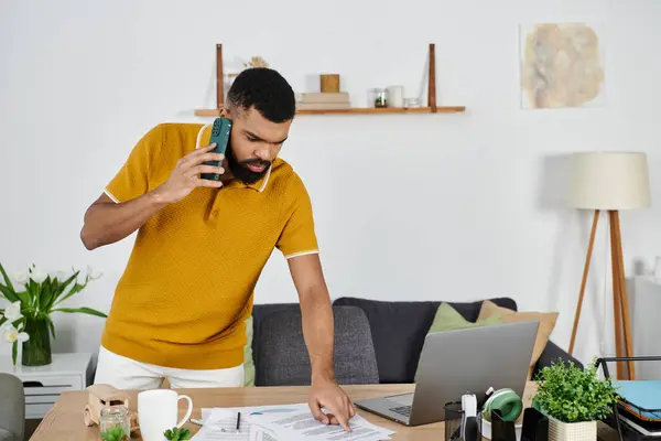 A man interacts on the phone while reviewing documents at his home workspace. — Stock Photo