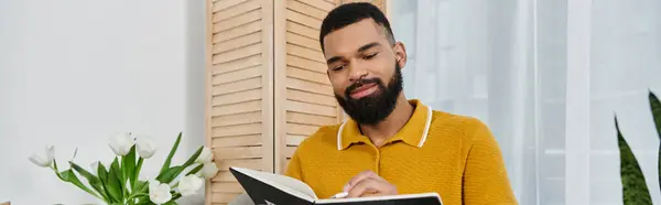 Man immersed in a book while relaxing in a bright, plant filled space. — Stock Photo