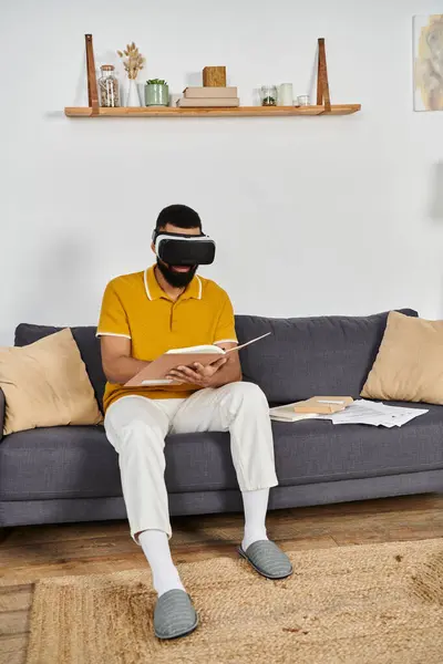 Relaxing at home, a man explores a virtual world with a book in hand. — Stock Photo