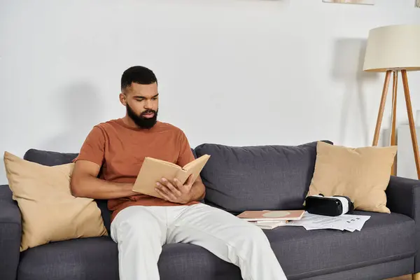 Un hombre guapo disfruta leyendo tranquilamente en casa en un cómodo sofá. - foto de stock