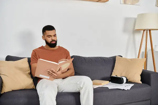 Un hombre se relaja en un sofá, inmerso en un libro en su acogedor espacio de vida. - foto de stock