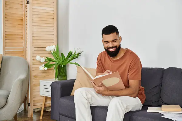A smiling man reads a book while seated comfortably at home. — Stock Photo