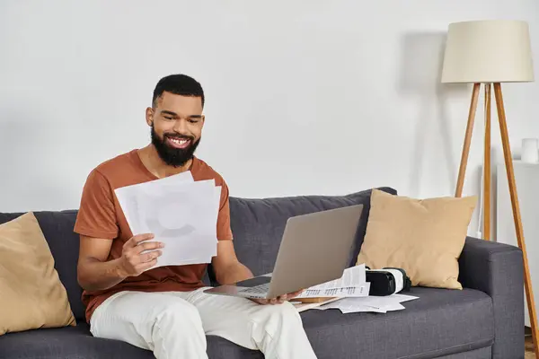 A cheerful man reviews documents on his laptop while seated comfortably. — Stock Photo
