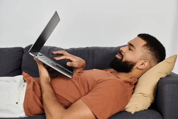 A handsome man enjoys leisure time while using his laptop at home. — Stock Photo