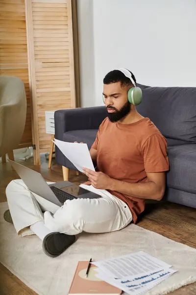 A man relaxes at home, focused on his laptop and notes, immersed in his work. — Stock Photo