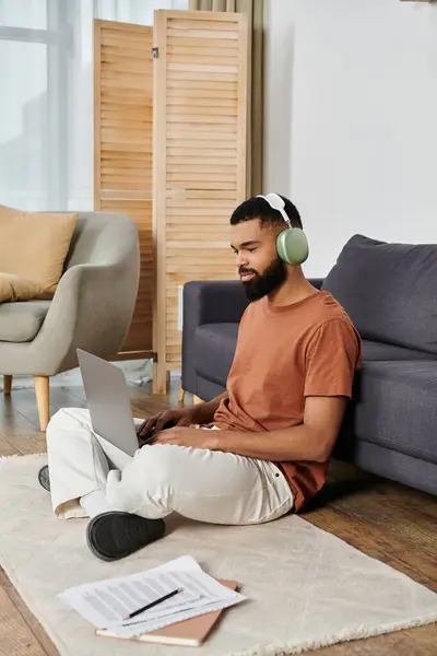 Uomo godendo di produttività mentre seduto sul pavimento con il suo computer portatile e cuffie. — Foto stock